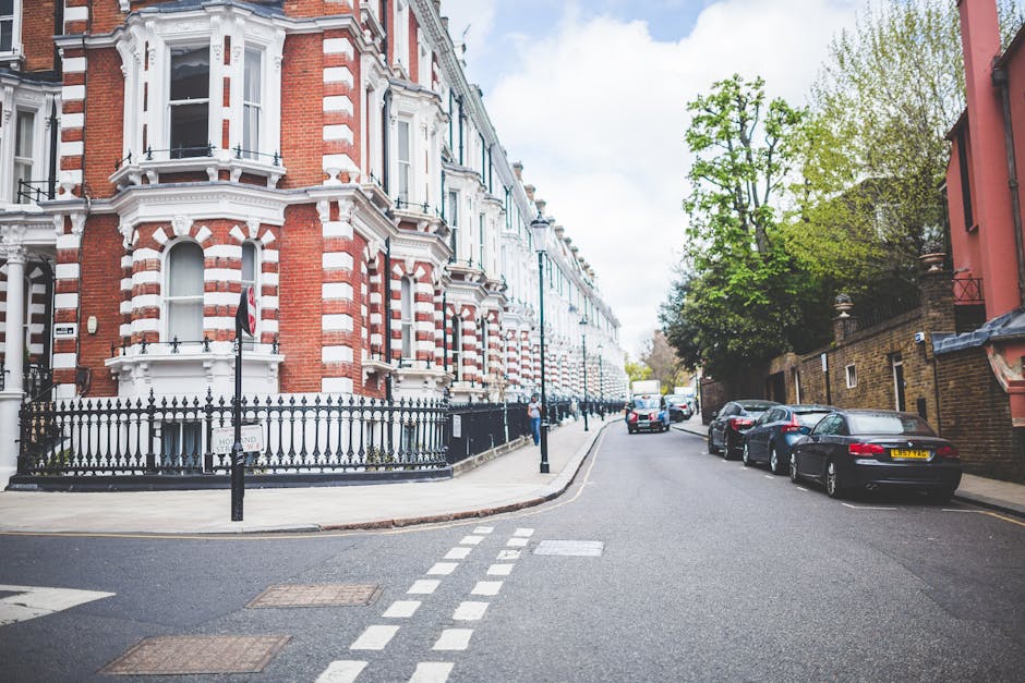 A quiet residential street in Earl's Court, featuring a row of Victorian-style terraced houses with red brick facades, white decorative trim, and bay windows. The buildings have black wrought-iron fen